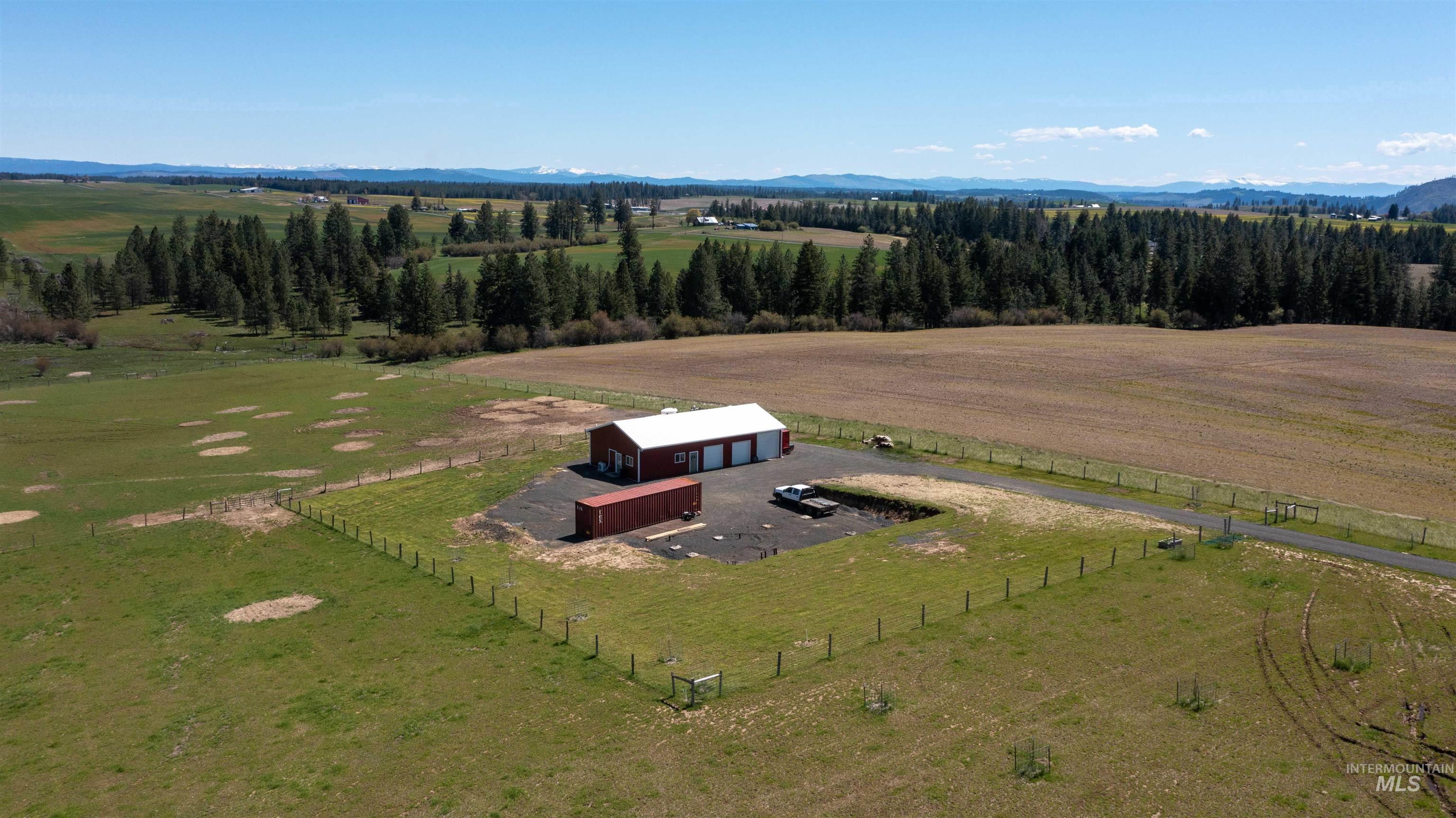 Expansive property featuring a red barn-style building with a white roof, a gravel driveway, and perimeter fencing