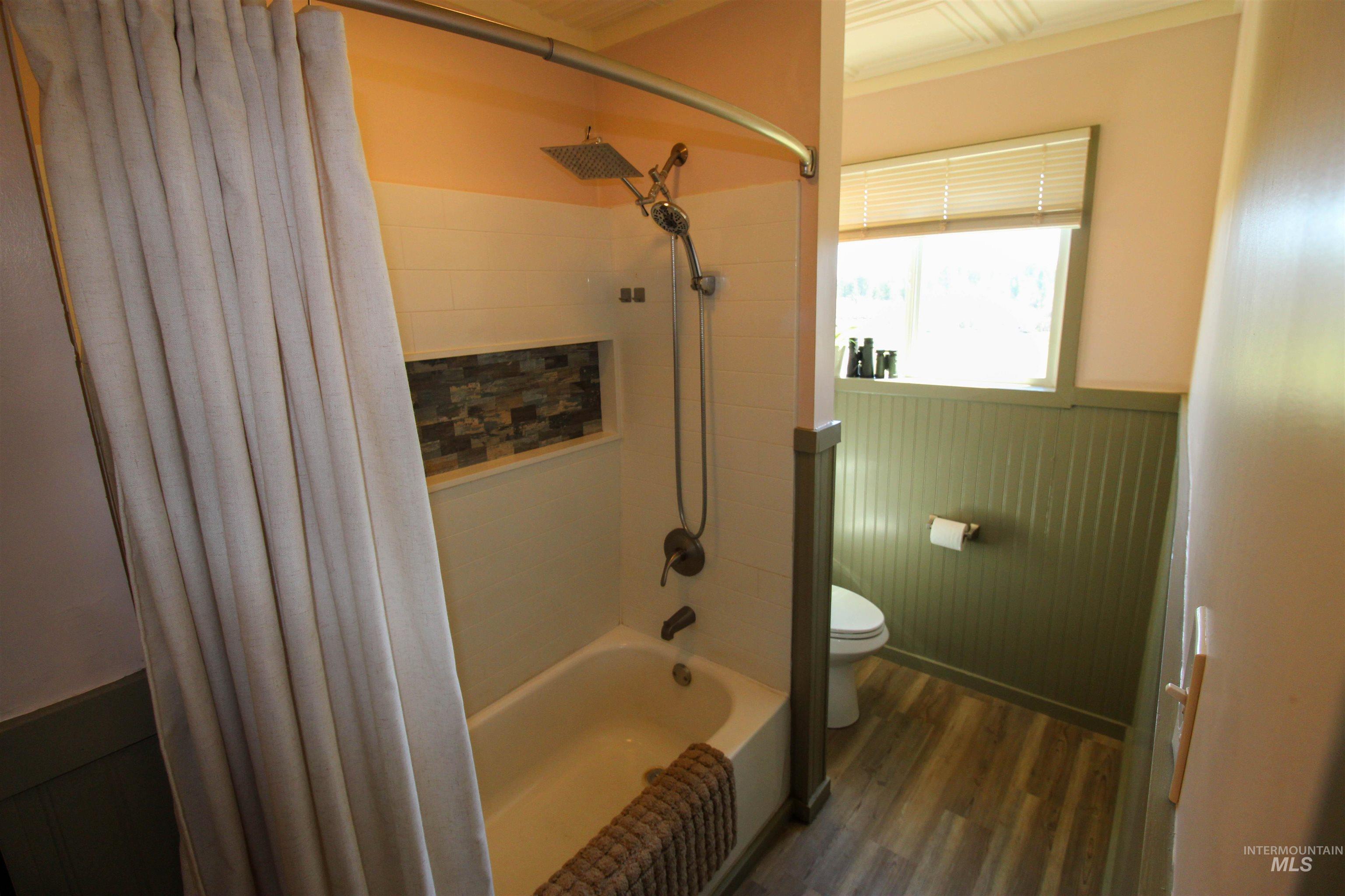 1254 Stuart Road Orofino, ID 83544 - Photo 11 of 48 Bathroom featuring a built-in tub with a shower system, a tiled shower niche, wood-finish flooring, beadboard wainscoting, and a window with blinds