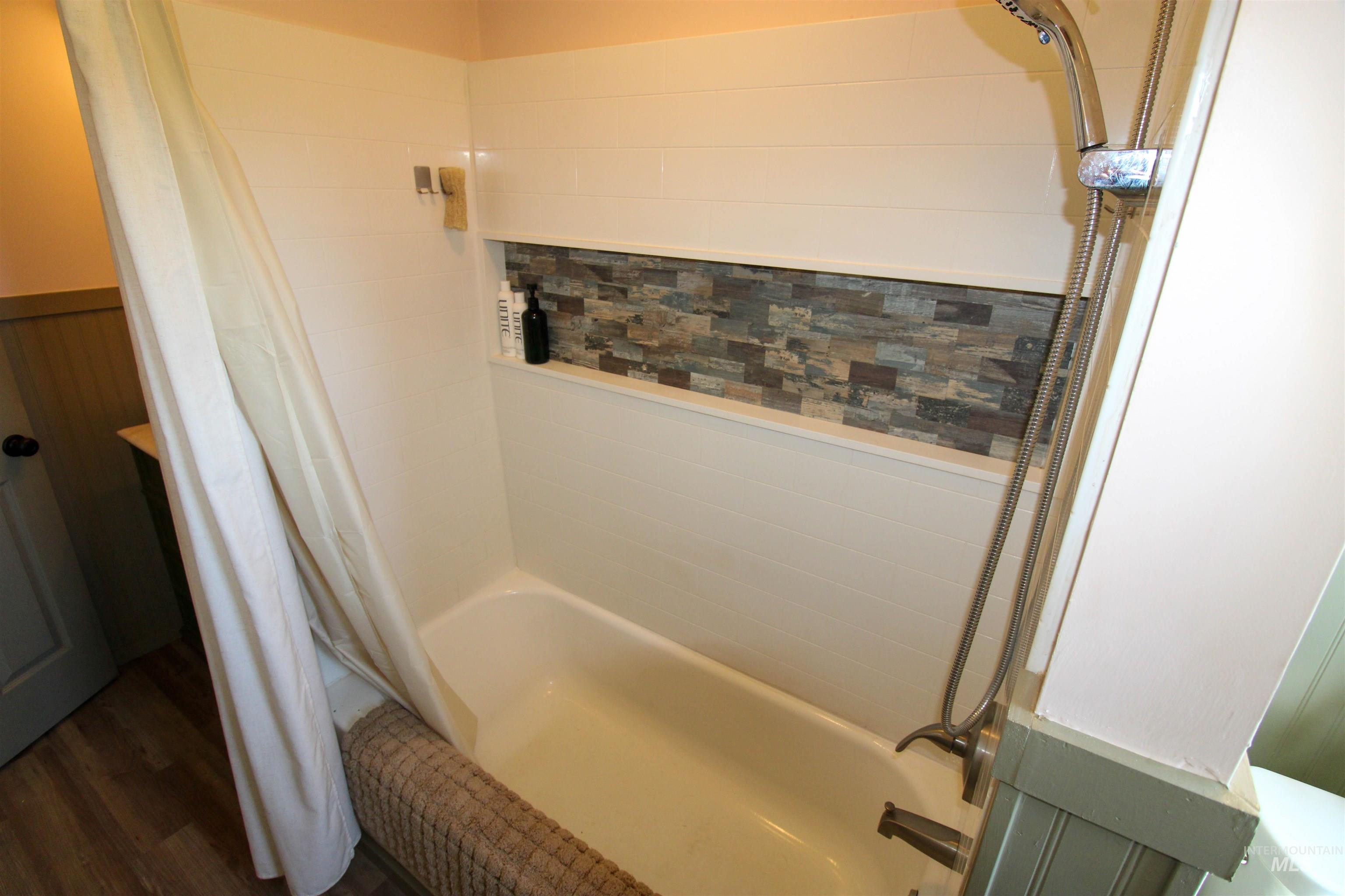 1254 Stuart Road Orofino, ID 83544 - Photo 12 of 48 Bathtub with a tiled niche featuring stacked stone accents, white subway tile surround, and a brushed nickel shower head with handheld sprayer