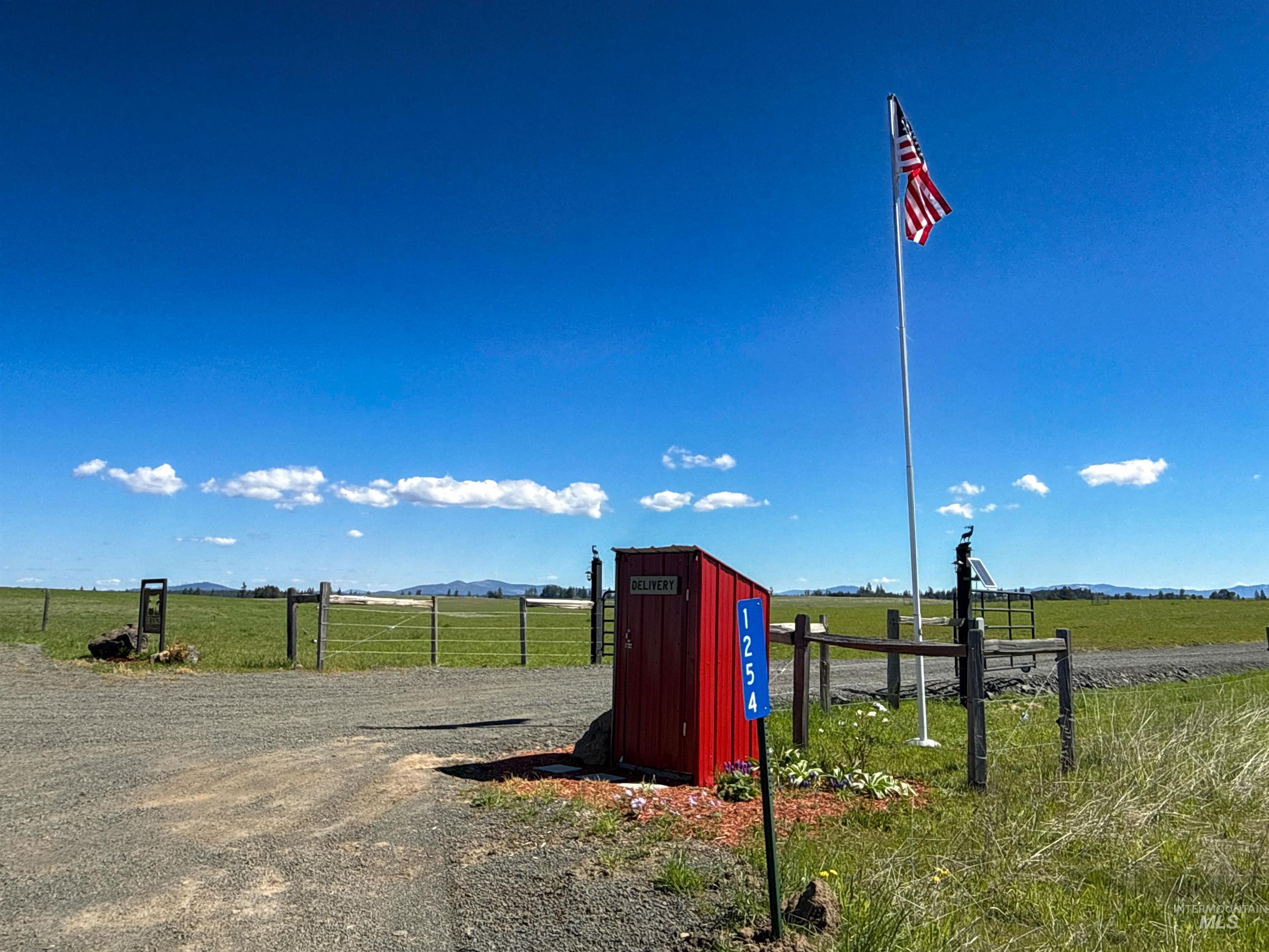 1254 Stuart Road Orofino, ID 83544 - Photo 3 of 48 Gravel driveway entrance featuring a red mailbox structure with visible address numbers, a tall flagpole, and a wooden fence line bordering a grassy field