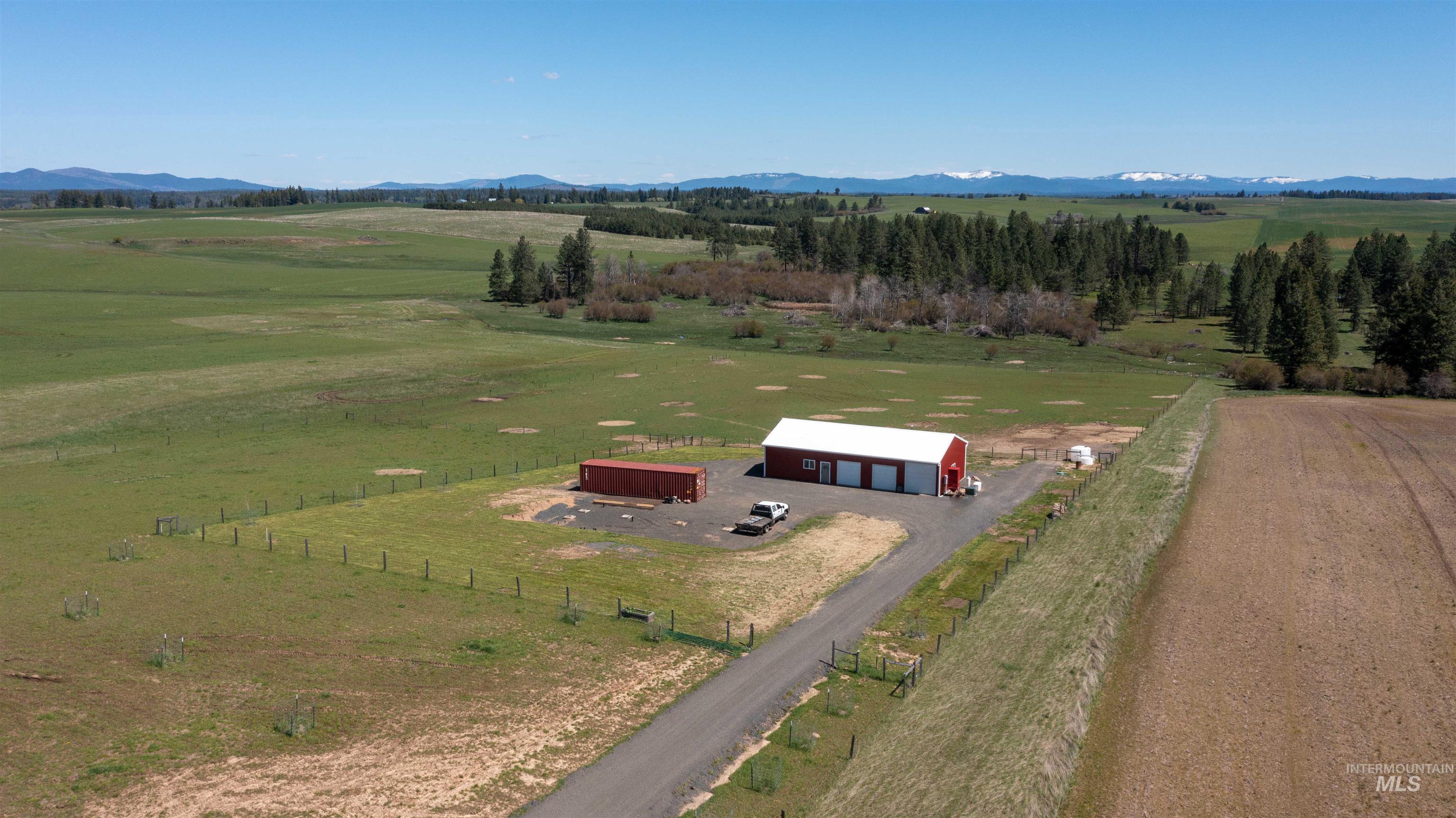 1254 Stuart Road Orofino, ID 83544 - Photo 37 of 48 Expansive agricultural landscape featuring a red barn with three garage doors and a white roof, a gravel driveway, and a red storage container