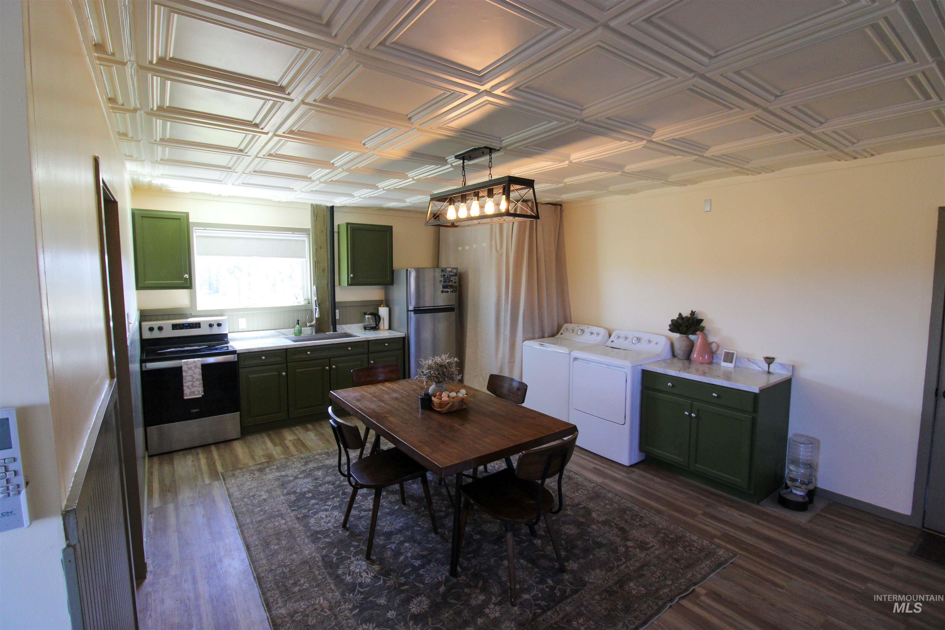1254 Stuart Road Orofino, ID 83544 - Photo 7 of 48 Open concept kitchen and laundry area featuring a pressed tin ceiling, wood-finish flooring, green cabinetry, and stainless steel appliances
