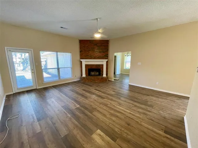 an empty room with wooden floor fireplace and windows