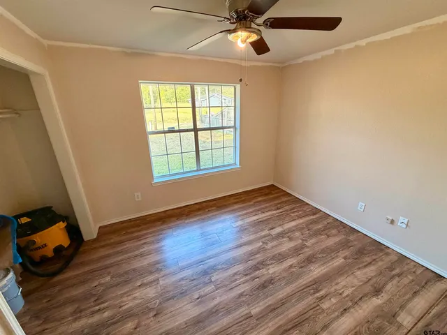 an empty room with wooden floor fan and windows