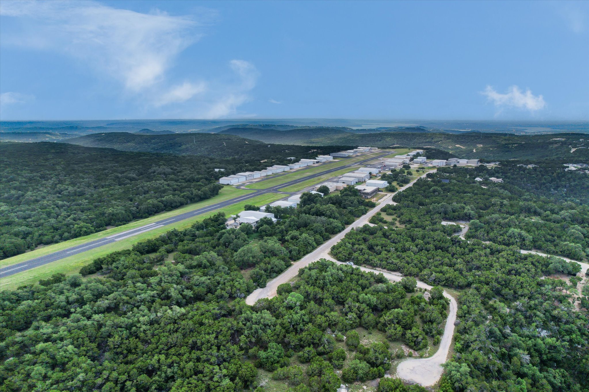 9404 Bar K Ranch Road Leander, TX 78645 - Photo 9 of 12 An aerial panorama reveals a private airstrip flanked by hangars, set amidst a sprawling, verdant landscape of hills.