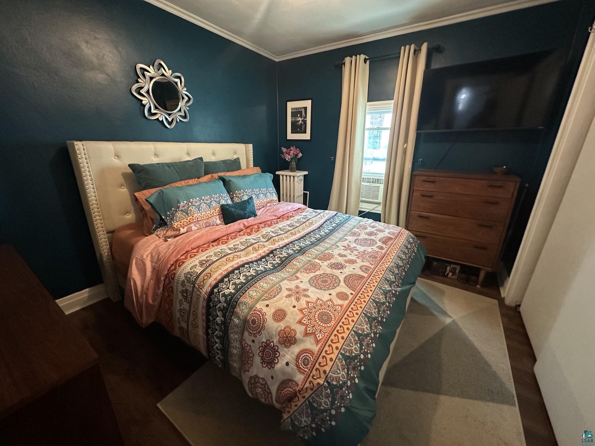 208 Chestnut Street Cloquet, MN 55720 - Photo 16 of 24 Bedroom featuring dark teal walls, white crown molding, wood-finish flooring, and a window with neutral-toned drapes