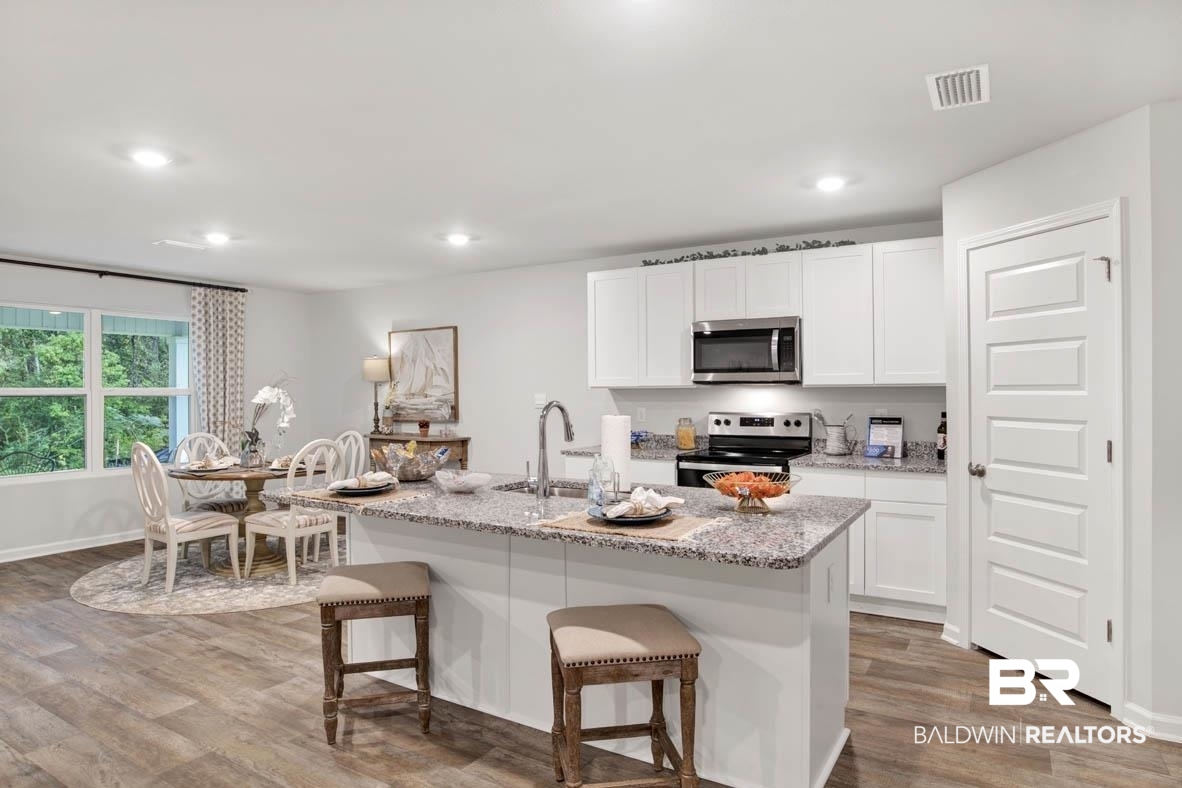 1235 Hayward Loop Foley, AL 36535 - Photo 15 of 26 Kitchen with a kitchen breakfast bar, wood-type flooring, a kitchen island with sink, stainless steel appliances, and white cabinetry