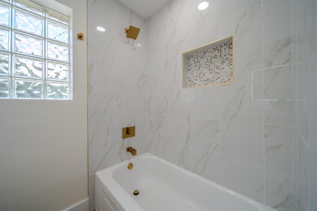 142 Ridgegate Drive Garland, TX 75040 - Photo 17 of 26 Tub and shower combination featuring white marble-look tile surround and gold-tone fixtures