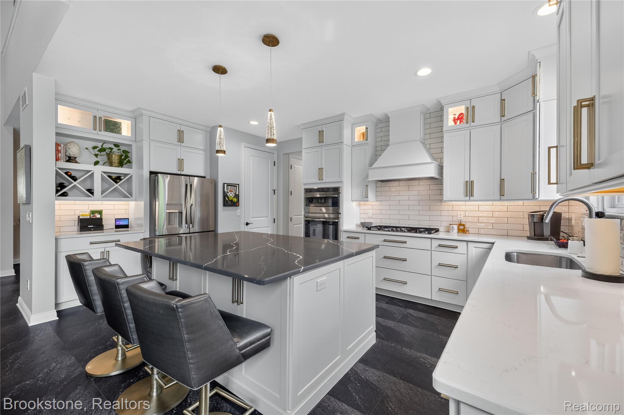 2167 Sanctuary Court Rochester, MI 48309 - Photo 5 of 68 Modern kitchen featuring a large island with dark stone countertop, white cabinetry with gold-toned hardware, stainless steel appliances, white subway tile backsplash, and dark wood-finish flooring