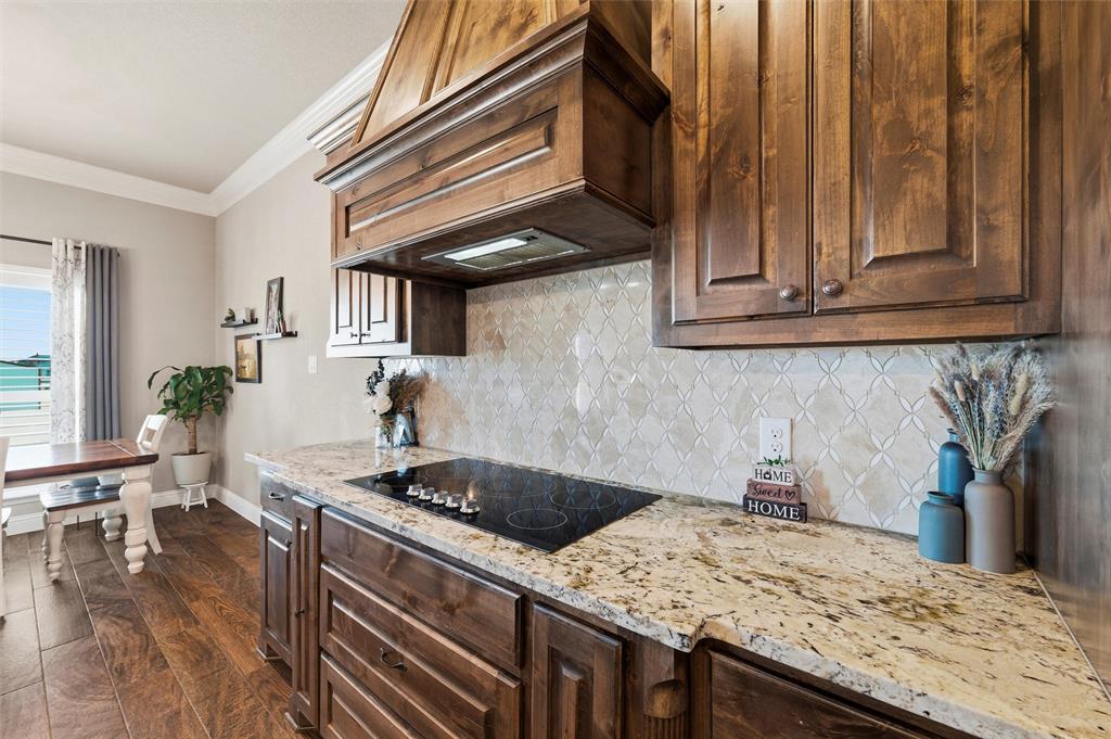 121 Bluff Ridge Court Paradise, TX 76073 - Photo 10 of 33 Kitchen featuring ornamental molding, dark brown cabinets, custom range hood, dark wood finished floors, and light stone countertops