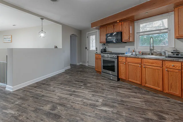 a large kitchen with kitchen island granite countertop wooden cabinets a stove a sink and a window