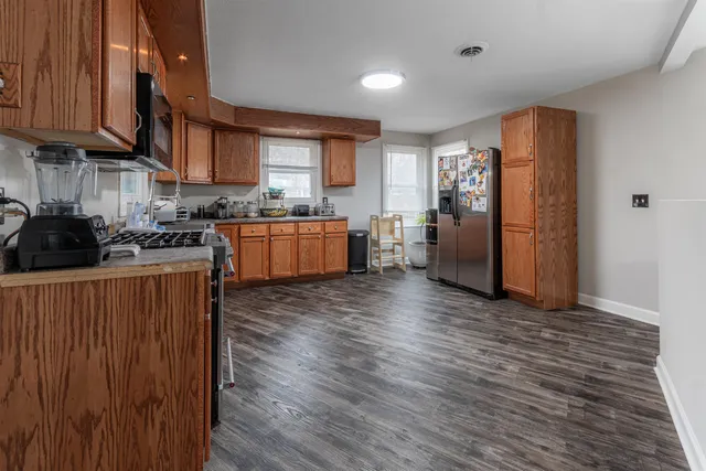 a kitchen with stainless steel appliances granite countertop wooden cabinets a refrigerator a sink a stove a microwave and wooden floors