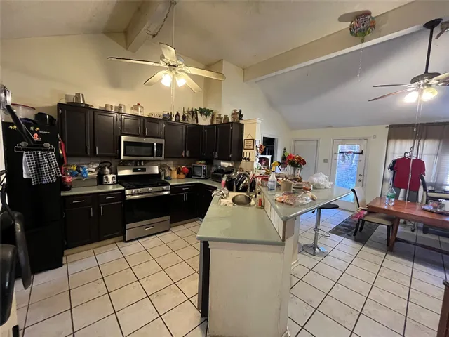 a kitchen with stainless steel appliances kitchen island granite countertop a refrigerator a sink dishwasher a dining table and chairs with wooden floor