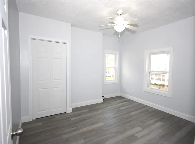 an empty room with wooden floor chandelier fan and windows