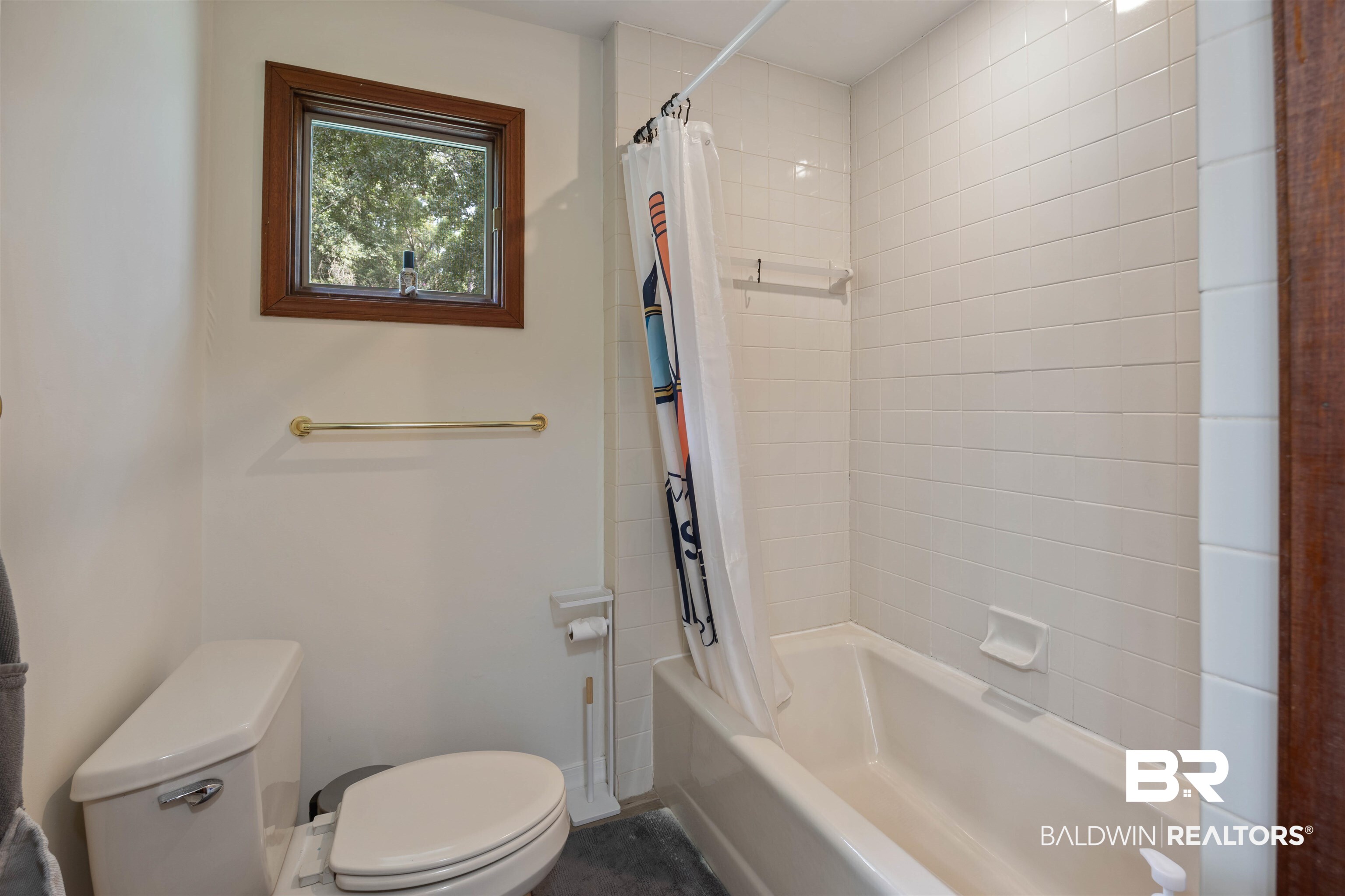 13677 Rebel Road Coden, AL 36523 - Photo 23 of 61 Bathroom featuring a white porcelain toilet, a gold-finish towel bar, a window with wood trim, and a shower-tub combination with white subway tile surround
