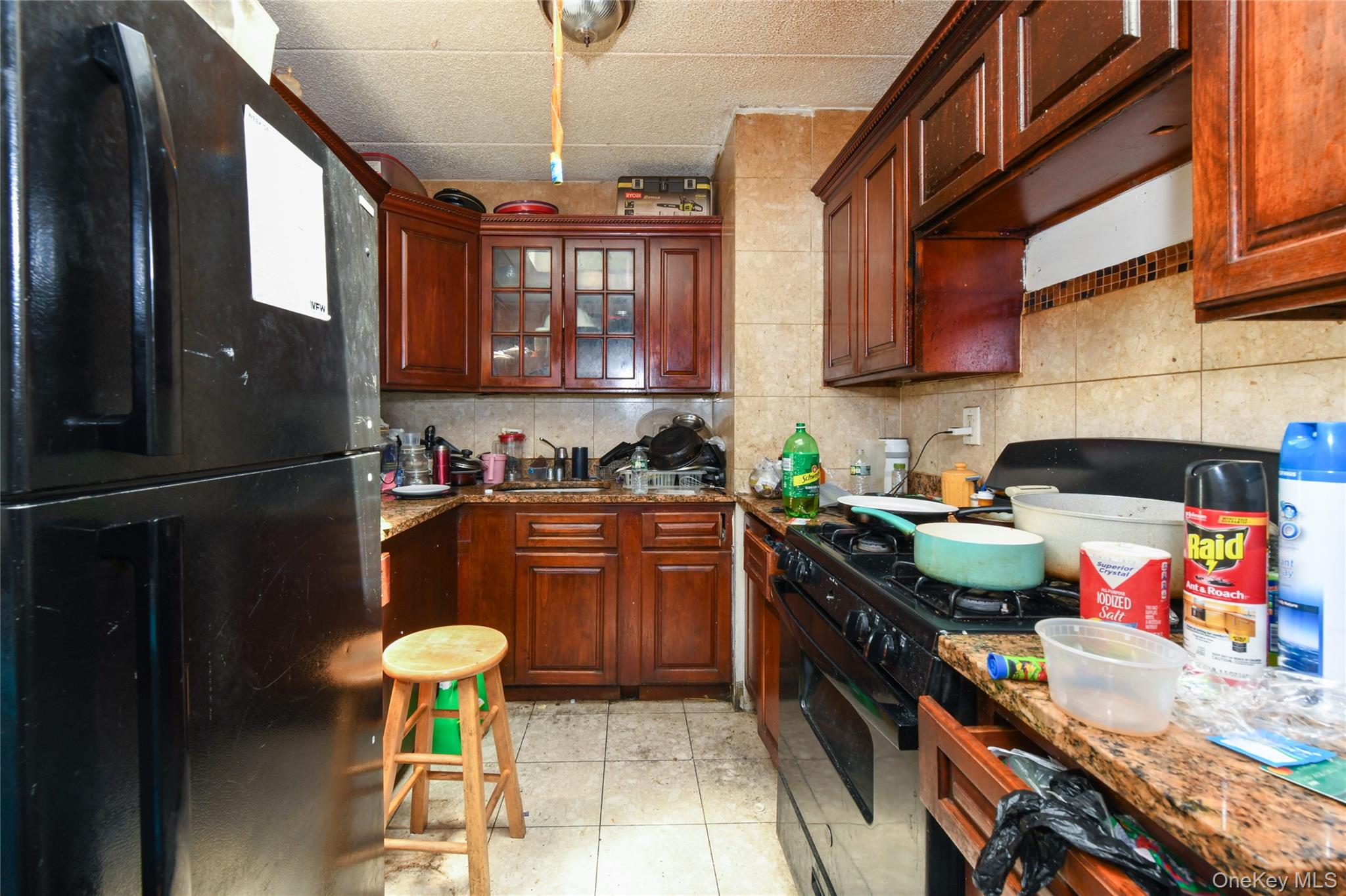 107-41 Sutphin Boulevard Queens, NY 11435 - Photo 12 of 19 Kitchen with black appliances, backsplash, dark stone countertops, light tile patterned flooring, and glass insert cabinets