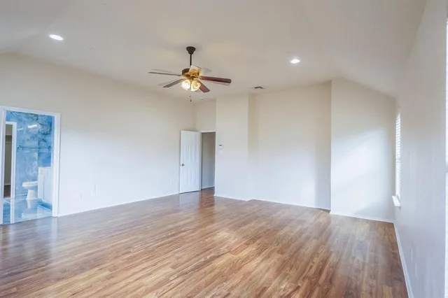 a view of an empty room with wooden floor and a ceiling fan
