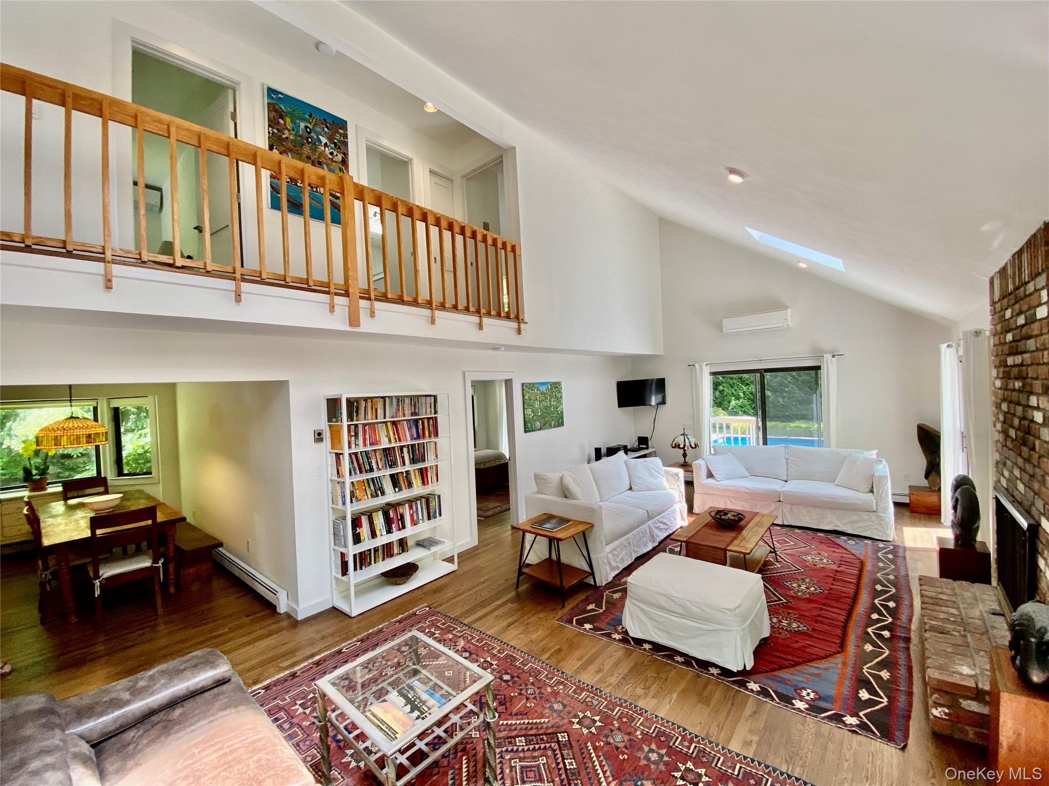 98 Hands Creek Road East Hampton, NY 11937 - Photo 2 of 20 Living room with a skylight, high vaulted ceiling, wood finished floors, and a wood burning fireplace.