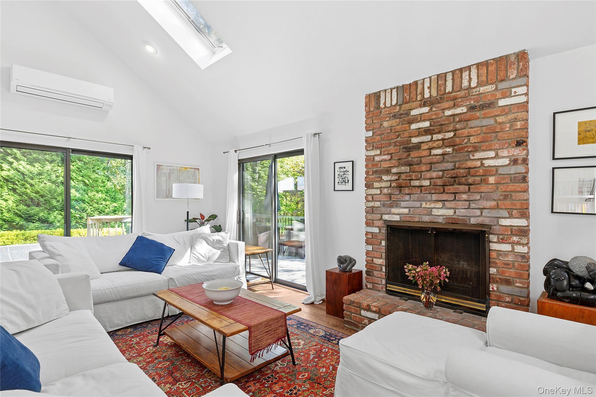98 Hands Creek Road East Hampton, NY 11937 - Photo 6 of 20 Living area featuring a skylight, wood finished floors, a wall mounted air conditioner, a fireplace, and high vaulted ceiling