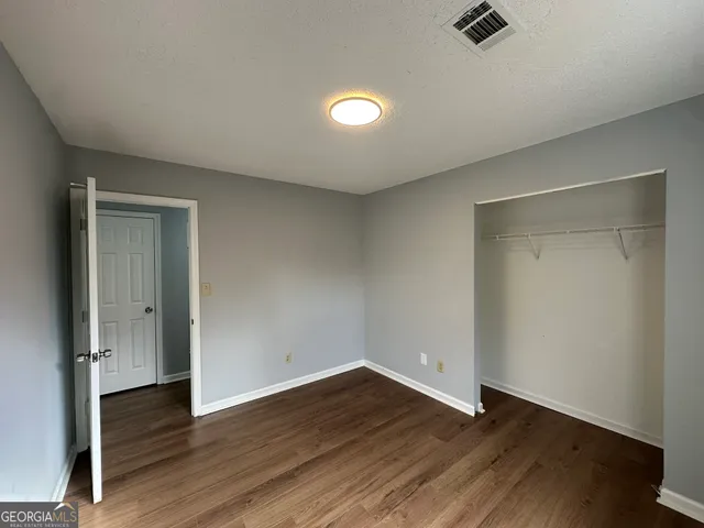 a view of an empty room with wooden floor and closet