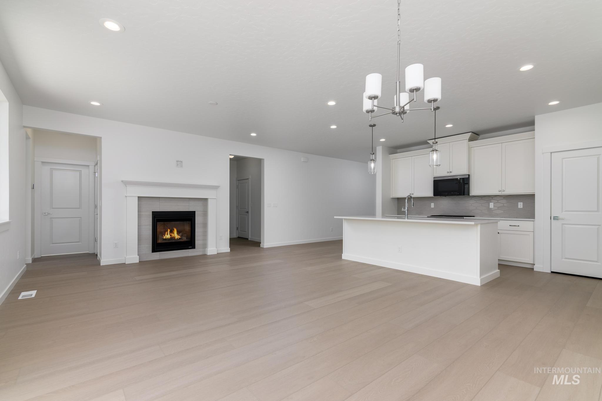 2040 West Blue Lightning Street Middleton, ID 83644 - Photo 7 of 8 Kitchen featuring open floor plan, white cabinets, a kitchen island with sink, a fireplace, and light wood finished floors