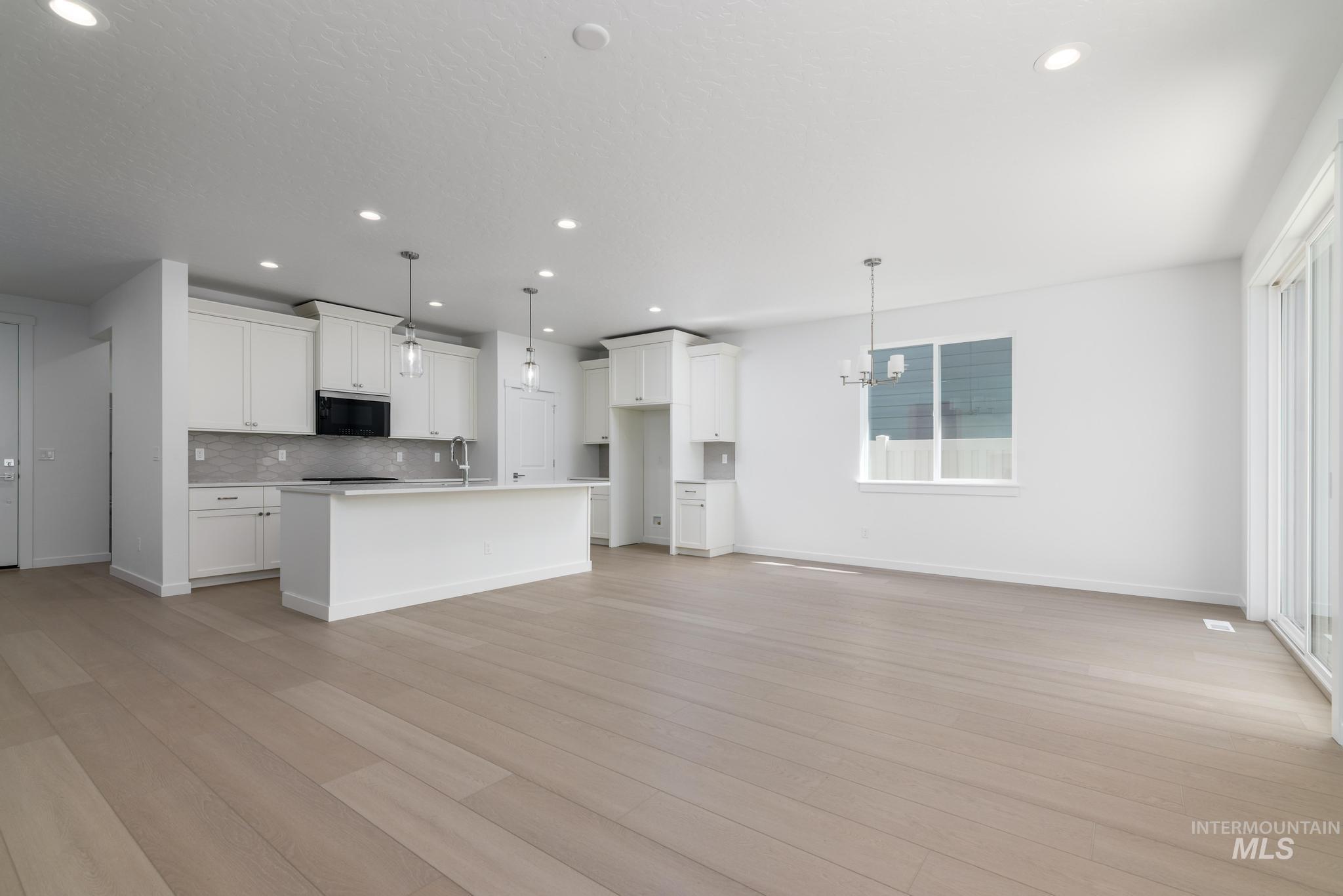 2040 West Blue Lightning Street Middleton, ID 83644 - Photo 8 of 8 Kitchen featuring open floor plan, an island with sink, white cabinets, hanging lights, and stainless steel microwave