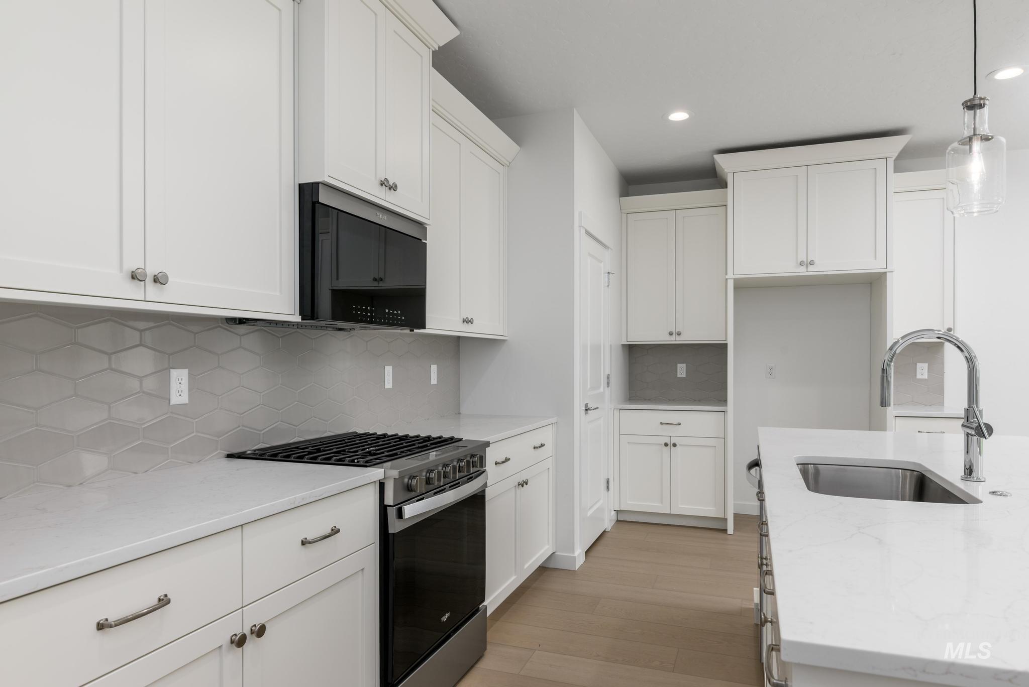 2040 West Blue Lightning Street Middleton, ID 83644 - Photo 3 of 8 Kitchen with gas range, white cabinets, light stone counters, black microwave, and decorative light fixtures