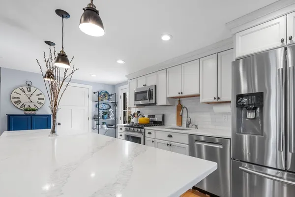 a kitchen with stainless steel appliances granite countertop a refrigerator a sink dishwasher a stove and white cabinets with wooden floor