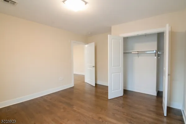 a view of an empty room with wooden floor & closet