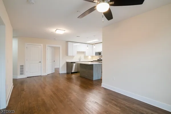 a view of an empty room and kitchen with wooden floor