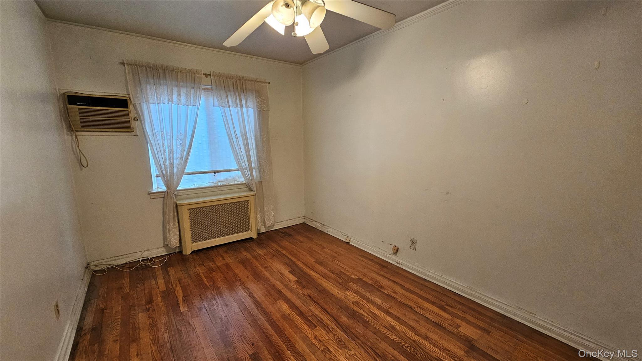108-11 65th Road Queens, NY 11375 - Photo 14 of 22 Unfurnished room featuring dark wood-style flooring, radiator, ceiling fan, and crown molding