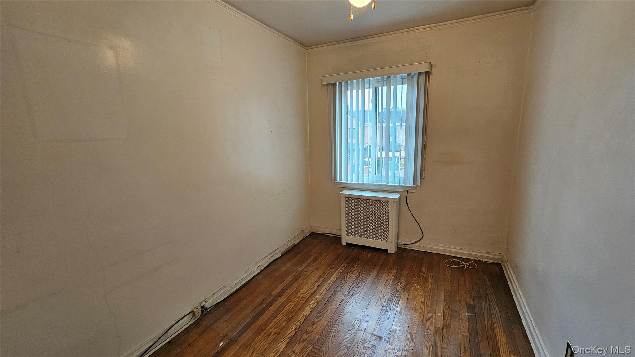 108-11 65th Road Queens, NY 11375 - Photo 16 of 22 Unfurnished room featuring dark wood finished floors, radiator heating unit, and crown molding