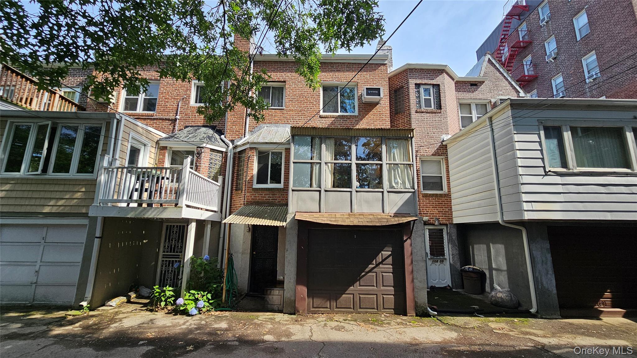 108-11 65th Road Queens, NY 11375 - Photo 22 of 22 View of front of home featuring an attached garage, brick siding, a balcony, and a chimney