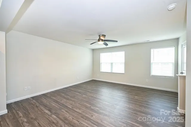 an empty room with wooden floor chandelier fan and windows