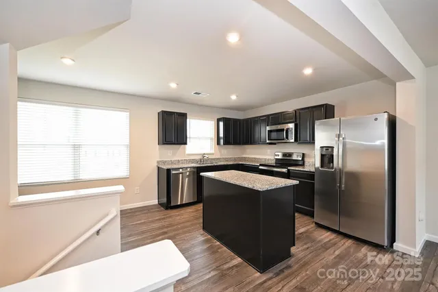 a kitchen with stainless steel appliances granite countertop a refrigerator a sink dishwasher a stove top oven a refrigerator and white cabinets with wooden floor
