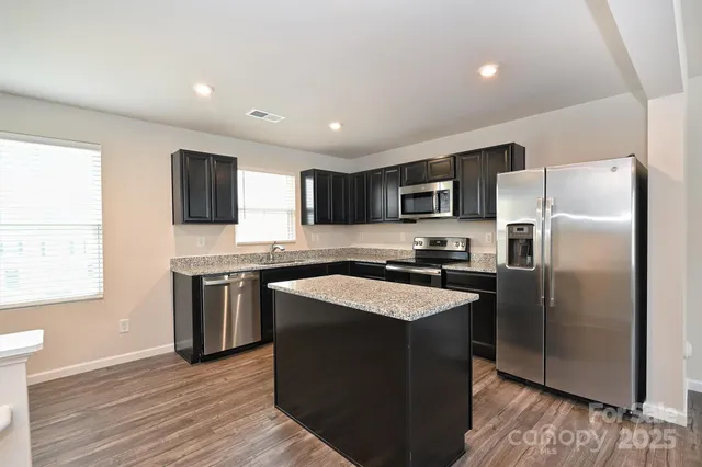 a large kitchen with a center island wooden floor stainless steel appliances and windows