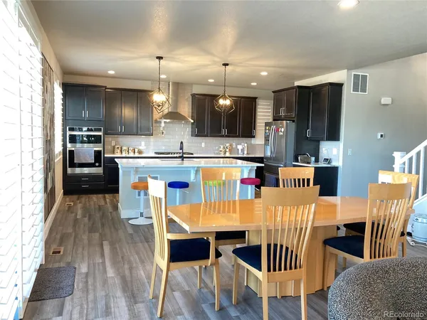a kitchen with stainless steel appliances kitchen island granite countertop a dining table chairs and a refrigerator