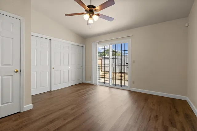 an empty room with wooden floor chandelier fan and windows
