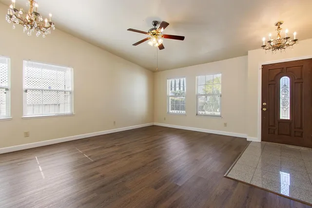 an empty room with wooden floor chandelier and windows