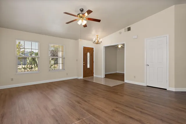 an empty room with wooden floor chandelier fan and windows