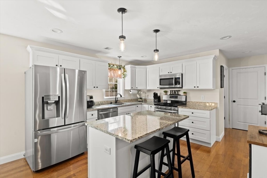 25 Upton Street Hanson, MA 02341 - Photo 7 of 30 a kitchen with stainless steel appliances granite countertop a refrigerator a stove a sink a dining table and chairs with wooden floor