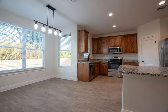 a kitchen with granite countertop wooden cabinets a stove a sink a refrigerator and a window