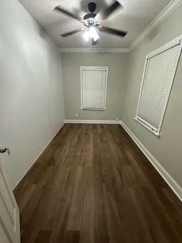 an empty room with wooden floor fan and windows