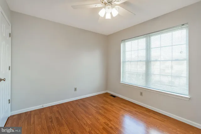 an empty room with wooden floor fan and windows