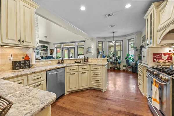 a kitchen with stainless steel appliances kitchen island granite countertop a stove top oven a sink a dining table and chairs with wooden floor