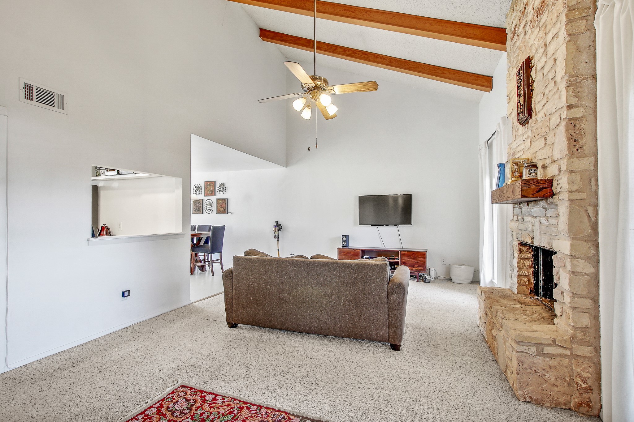 8925 North Plaza, Unit 69 Austin, TX 78753 - Photo 6 of 29 Living room with a ceiling fan, beam ceiling, carpet floors, high vaulted ceiling, and a stone fireplace