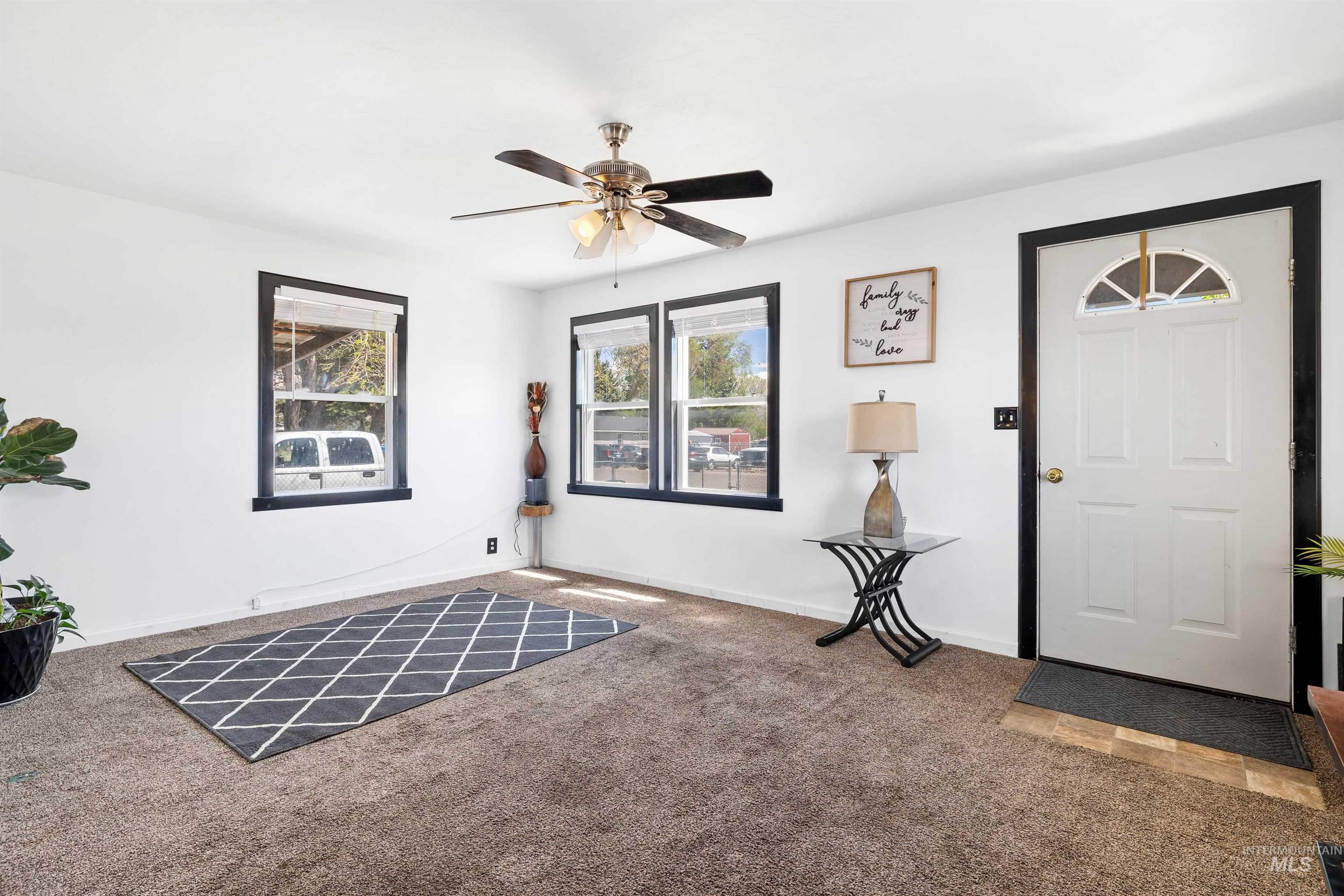 102 East 6th Street Rupert, ID 83350 - Photo 6 of 27 Spacious room featuring neutral carpeting, white walls, multiple windows with black trim, and a ceiling fan with integrated lighting