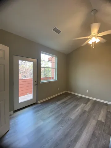 an empty room with wooden floor fan and windows
