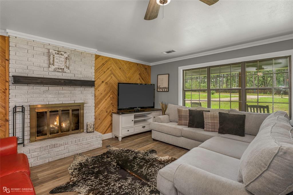 1426 Caney Lake Road Minden, LA 71055 - Photo 4 of 36 Spacious living area featuring a whitewashed brick fireplace with a dark wood mantle, wood-finish flooring, a chevron wood accent wall, and large windows overlooking the grounds
