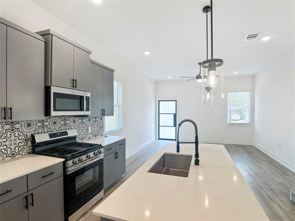 6107 Begonia Circle, Unit 2 Austin, TX 78741 - Photo 4 of 15 Kitchen with appliances with stainless steel finishes, gray cabinets, a kitchen island with sink, hanging light fixtures, and tasteful backsplash